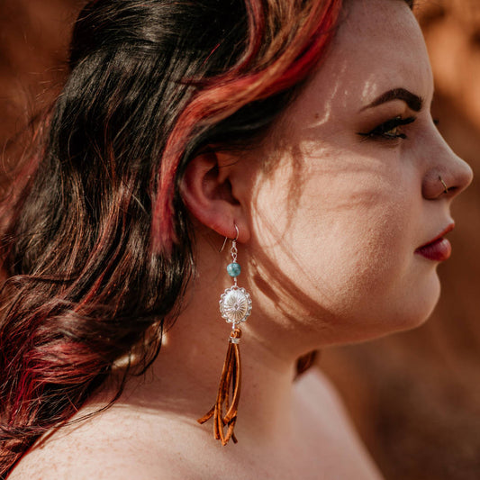 A dark haired model wearing silver, turquoise, and leather fringe earrings